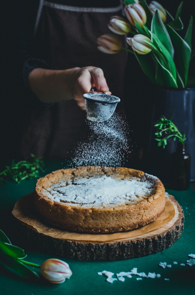 dusting powdered erythritol on a vegan coconut millet cake